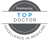 The image displays a stylized badge with the text FINDATOP DOCTOR at the top, followed by TOP DOCTOR in bold letters. Below this, there is an emblem indicating a challenge or competition, and further down, the words CHALLENGE OF THE YEAR are visible. The background of the badge features a blue circular design with a white border. At the bottom of the image, there s a graphic element resembling a doctor s stethoscope in black and white.