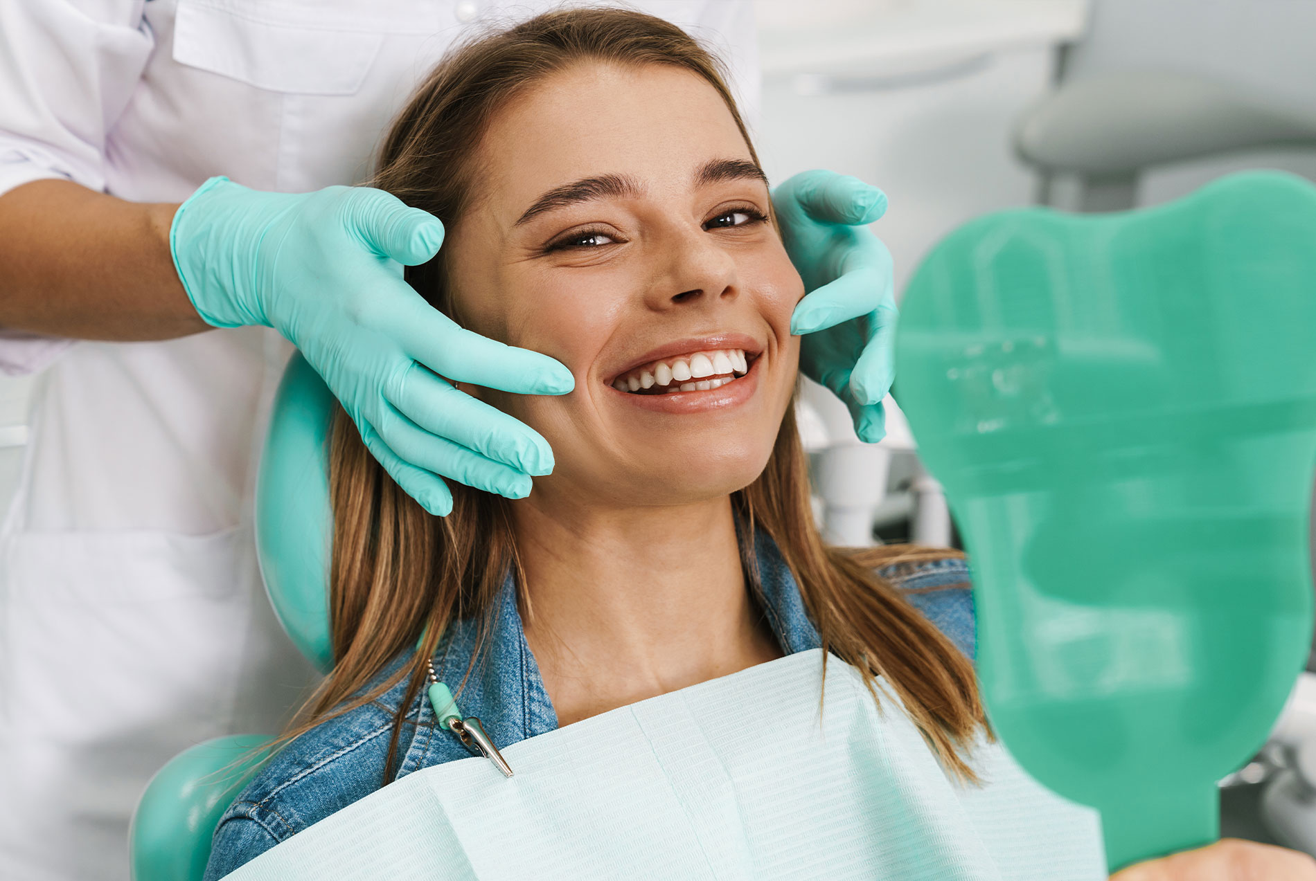 A young woman sitting in a dental chair receiving dental care from a dentist, with her smiling face.