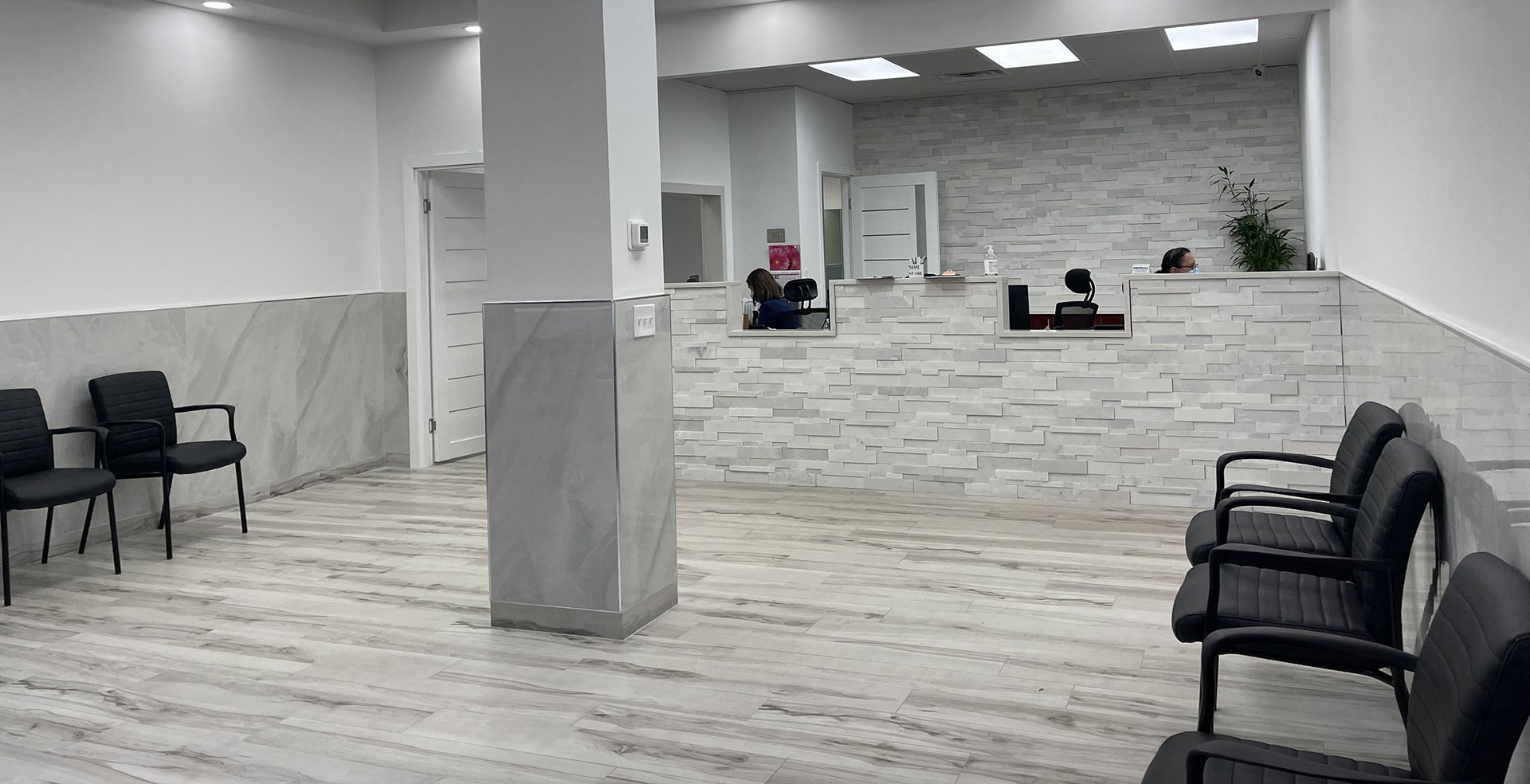 A modern waiting room with a clean, minimalist design featuring light wooden flooring, white walls, and gray tiles.